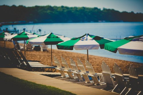Beach scene with green and white umbrellas, lounge chairs, and calm water in the background.