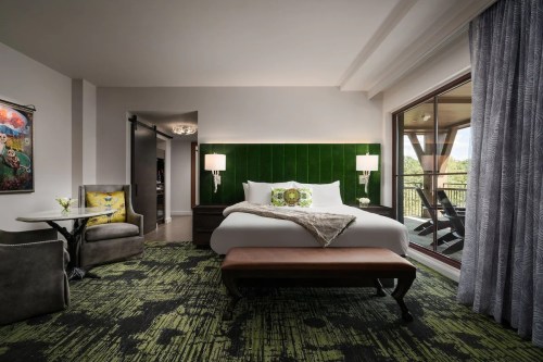 A modern hotel room featuring a green accent wall, a king bed, seating area, and large windows with natural light.