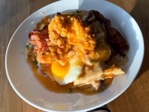 A bowl of breakfast featuring fried chicken, sunny-side-up eggs, and gravy over a bed of potatoes.