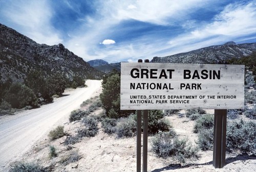 Sign for Great Basin National Park with a dirt road and mountains in the background under a blue sky.