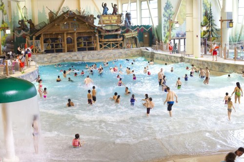 A busy indoor water park with families enjoying the wave pool and water features. Colorful decor and playful atmosphere.