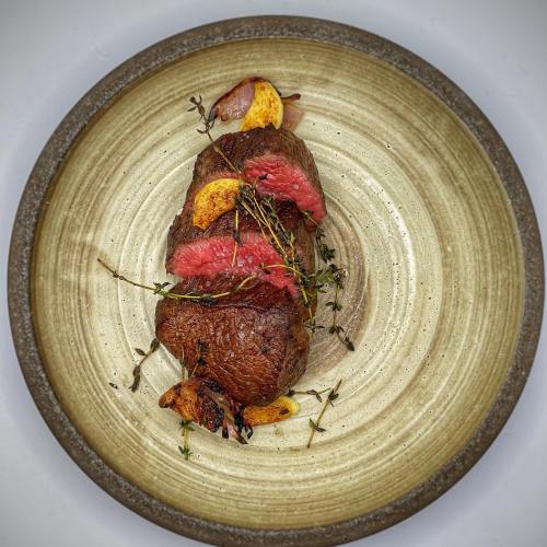 A beautifully plated roast beef with herbs and caramelized onions on a rustic ceramic plate.
