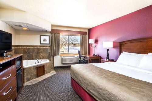 Cozy hotel room featuring a king bed, a jetted tub, a desk, and a large window with a view.