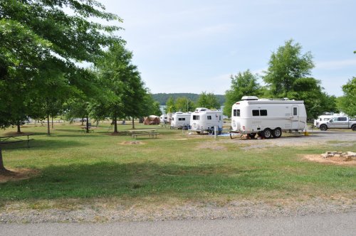 A grassy campground with several RVs parked under trees, surrounded by a peaceful landscape.