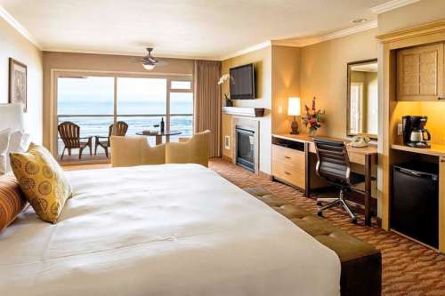Cozy hotel room with a king bed, desk, and seating area, featuring ocean views through large windows.
