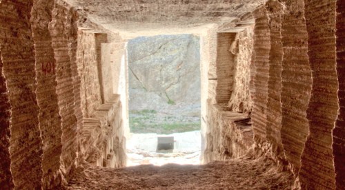 View from inside a stone tunnel, leading to a bright opening with rocky walls and greenery visible outside.