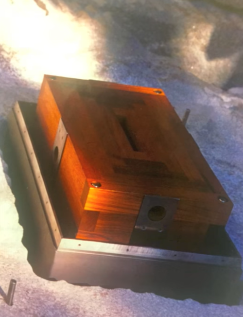 A wooden box with metal accents, resting on a textured surface, illuminated by soft light.