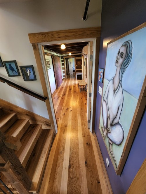 A hallway with wooden floors, featuring a colorful painting on the wall and stairs leading down.