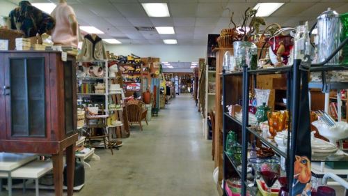 A wide aisle in a vintage store filled with various antiques and collectibles on shelves and tables.