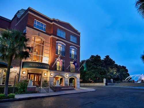 A brick building with "Harbour View" signage, palm trees, and flags, set against a twilight sky.