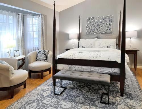 Cozy bedroom featuring a four-poster bed, armchairs, a bench, and elegant decor in soft gray tones.