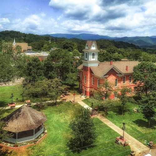 A scenic view of a park with a gazebo and historic building, surrounded by trees and mountains in the background.