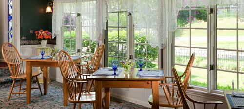 Bright dining area with wooden tables, blue glassware, and lace curtains, surrounded by lush greenery outside.