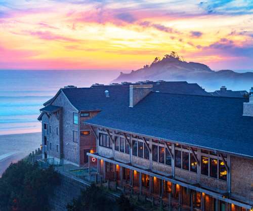 A coastal hotel at sunset, with vibrant colors in the sky and a distant island silhouette over the ocean.