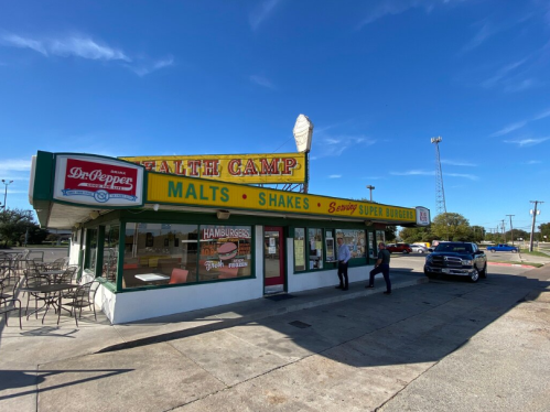 A colorful diner named "Health Camp" with outdoor seating, serving malts and shakes, under a clear blue sky.