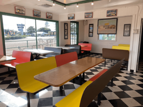 Colorful diner interior with checkered floor, featuring booths and tables, large windows, and vintage decor.