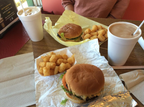 A table with two burgers, a side of tater tots, and two drinks in cups, set in a casual dining environment.