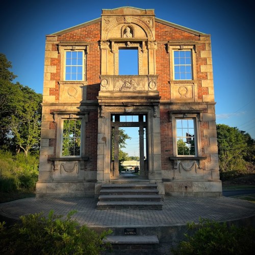 A partially collapsed brick building with ornate details, featuring empty window frames and a clear blue sky.