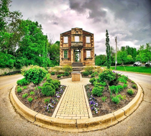 A historic building with a stone facade surrounded by a circular garden and cloudy skies.