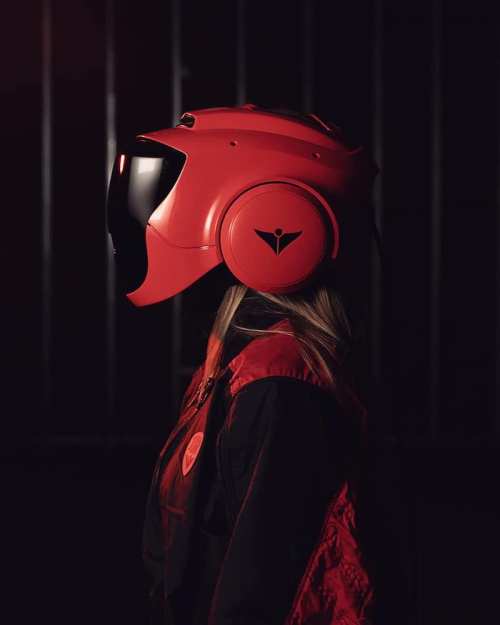 A profile view of a person wearing a sleek red helmet and a matching jacket against a dark background.