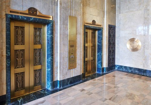 Art Deco-style elevator doors in a marble lobby with decorative accents and a vintage elevator panel.