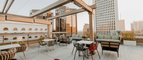 Rooftop terrace with modern furniture, overlooking city buildings at sunset.