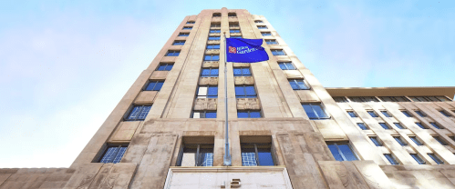 Art Deco building with a blue flag, featuring intricate stonework and large windows, against a clear sky.