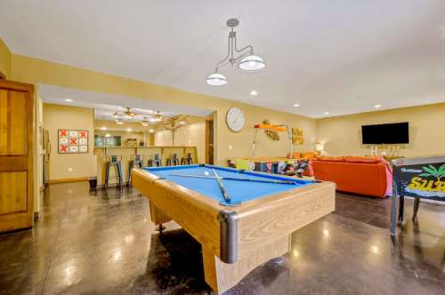 A spacious game room featuring a blue pool table, cozy seating, and a modern decor with warm lighting.