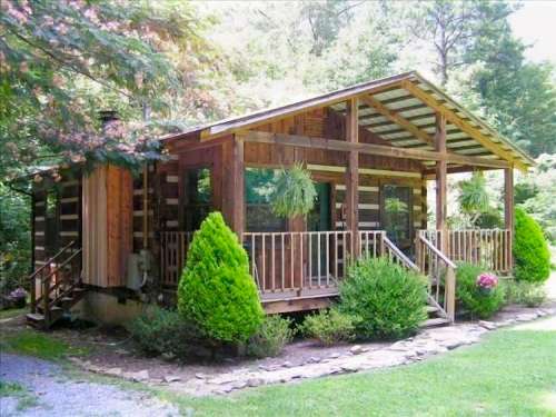 A cozy wooden cabin surrounded by greenery, featuring a porch and lush plants in a serene outdoor setting.