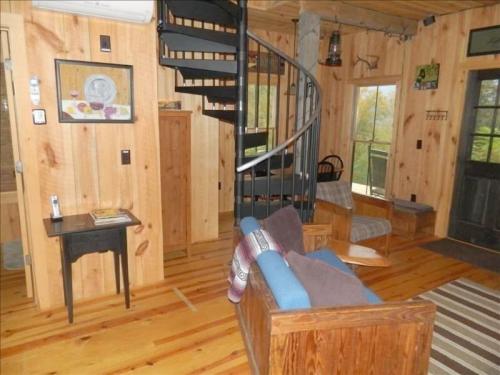 Cozy wooden interior with a spiral staircase, seating area, and large windows showcasing a natural view.