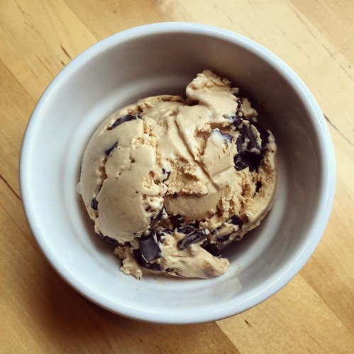 A bowl of creamy ice cream with chocolate chunks on a wooden surface.