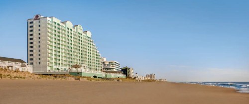 A beachfront hotel with a green facade stands alongside a sandy beach under a clear blue sky.