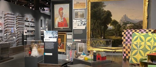 A museum exhibit featuring various artworks, artifacts, and informational displays in a well-lit space.