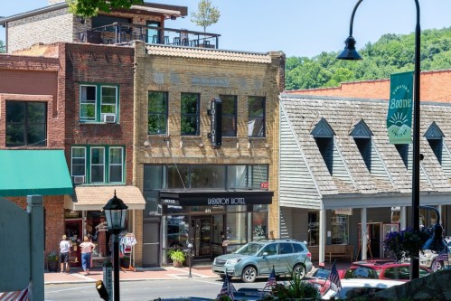 Historic buildings line a street, featuring the Yost Hotel and shops, with greenery in the background and flags displayed.