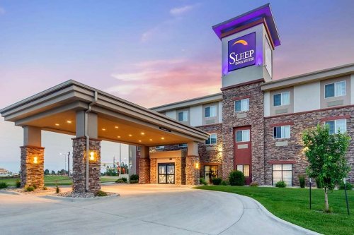 Exterior view of a Sleep Inn & Suites hotel at sunset, featuring a stone entrance and well-maintained landscaping.