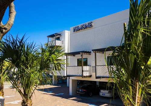 A modern building with the name "SIMONE" displayed, surrounded by palm trees and clear blue skies.
