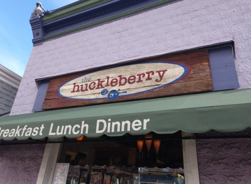 Sign for "The Huckleberry" restaurant, featuring a wooden design and the words "Breakfast Lunch Dinner" below.