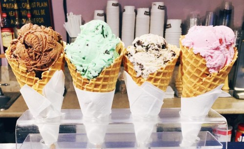 Four ice cream cones in waffle cups: chocolate, mint chocolate chip, cookies and cream, and strawberry.