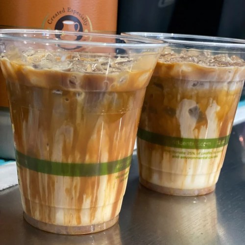 Two clear cups filled with iced coffee, layered with cream and caramel drizzle on top.