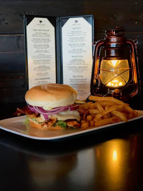 A delicious burger with bacon, cheese, and onions, served with fries, next to a glowing lantern and menu in the background.
