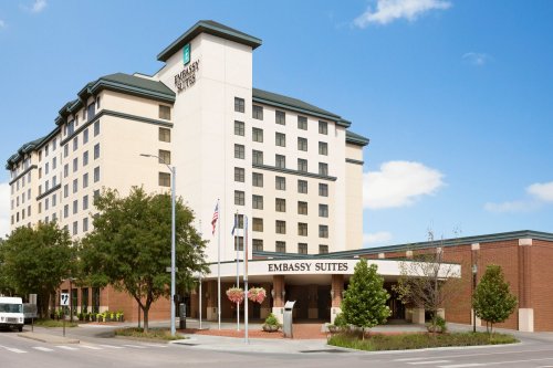 Exterior view of an Embassy Suites hotel with a modern design, featuring a welcoming entrance and clear blue sky.