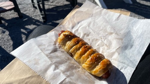 A golden-brown pastry wrapped around a hot dog, resting on crumpled parchment paper.