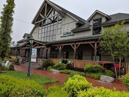 L.L. Bean Hunting & Fishing store with a wooden facade, surrounded by greenery and colorful kayaks outside.