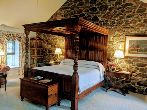 Cozy bedroom featuring a wooden four-poster bed, stone walls, and warm lighting.
