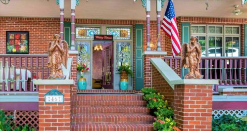 A charming brick porch with decorative angels, potted flowers, and an American flag, featuring stained glass windows.