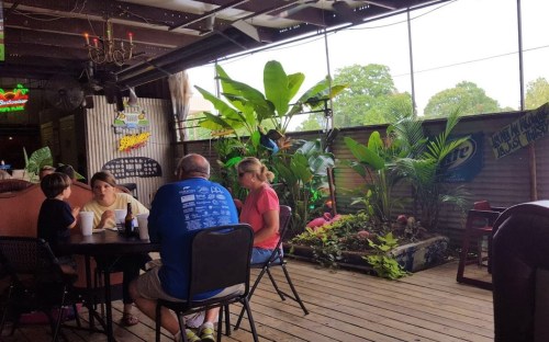 A casual dining area with plants, featuring a family at a table enjoying drinks in a relaxed atmosphere.