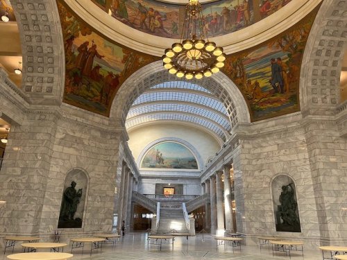 Interior of a grand hall with marble walls, ornate ceiling, large chandelier, and colorful murals.