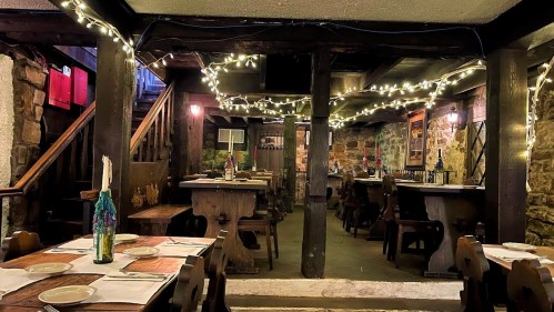 Cozy restaurant interior with wooden tables, stone walls, and string lights creating a warm ambiance.