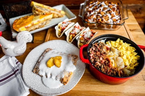 A colorful spread of breakfast dishes, including tacos, a casserole, and a plate with pancakes topped with fruit and cream.