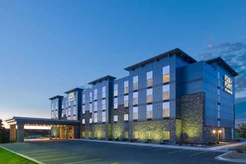 Modern hotel exterior at dusk, featuring a four-story building with large windows and a welcoming entrance.